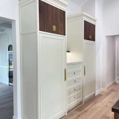 Tall white pantry cabinets and refrigerator panels with oversized gold handles and dark wood upper accents.
